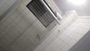 Une salle de bain avec une douche à parois de verre, des murs recouverts de carreaux blancs et des toilettes blanches.