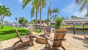 Un espacio al aire libre con sillas Adirondack, una chimenea y vistas a un puerto deportivo con barcos.