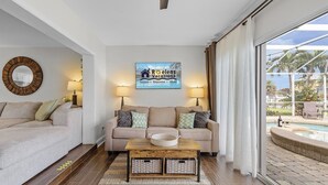 Una sala de estar con un sofá color beige, dos lámparas, una mesa de centro y un cartel de Roelens Vacations.