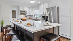 Una cocina moderna con armarios blancos, electrodomésticos de acero inoxidable y una isla central con taburetes de bar.