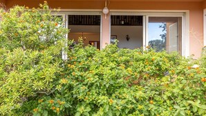 En byggnad med en balkong och en trädgård med grönt lövverk och orange blommor.
