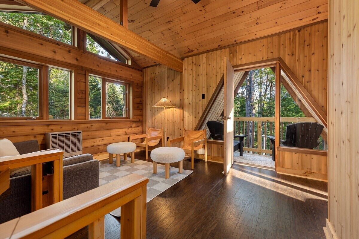 Ein Interieur einer Holzhütte mit einer gemütlichen Sitzecke, großen Fenstern und einer Treppe, die zu einer Außenterrasse führt.