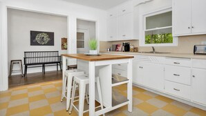 Cozinha com armários brancos, bancada de madeira e chão quadriculado.