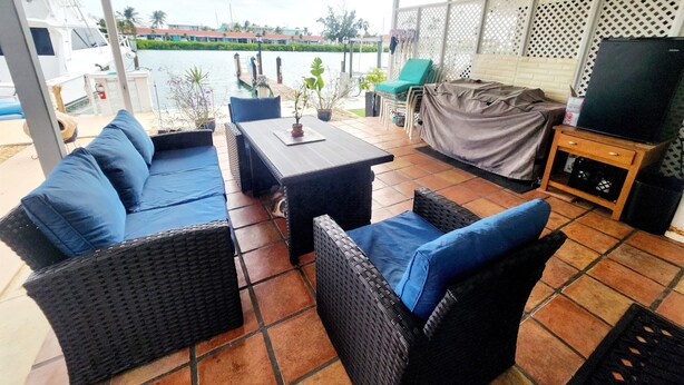 A covered outdoor seating area with wicker furniture, a table, and a TV on a wooden stand. - Key Colony Beach House with Cabana Club membership (Key Colony Beach)