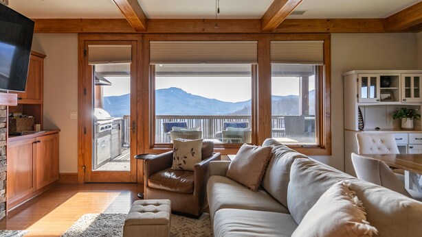 Un soggiorno spazioso con una grande finestra che offre vista sulle montagne, una ventola a soffitto e una cucina visibile attraverso la finestra.