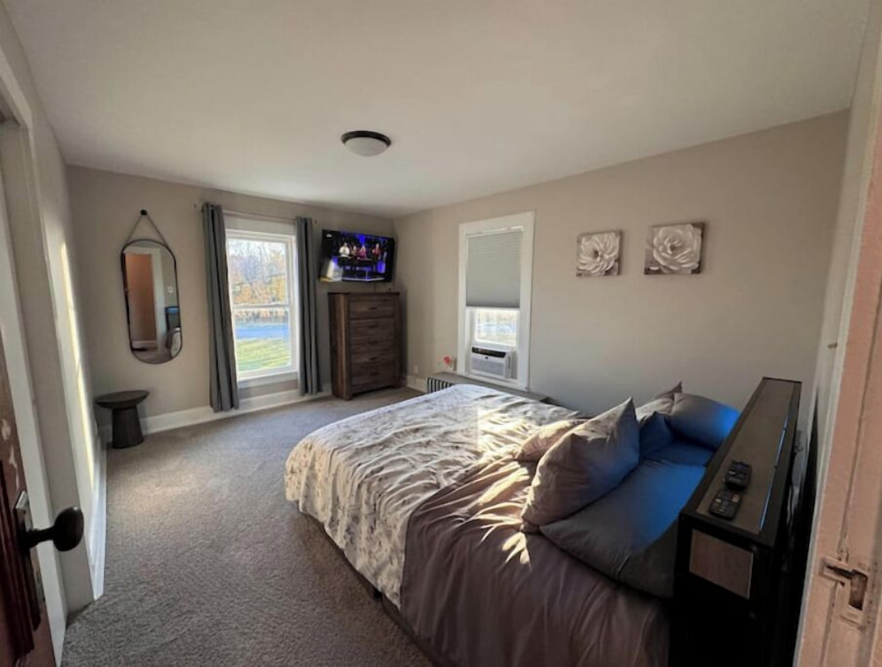 A bedroom with a bed, a dresser, a television, and a window.