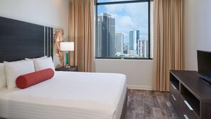 Habitación de hotel con una cama grande, televisión, mesita de noche y ventana con vista a la ciudad.