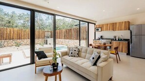 A modern living room with a sofa, coffee table, and a view of a pool and garden. - Beautiful 2 Bedroom Apartment (Tulum)
