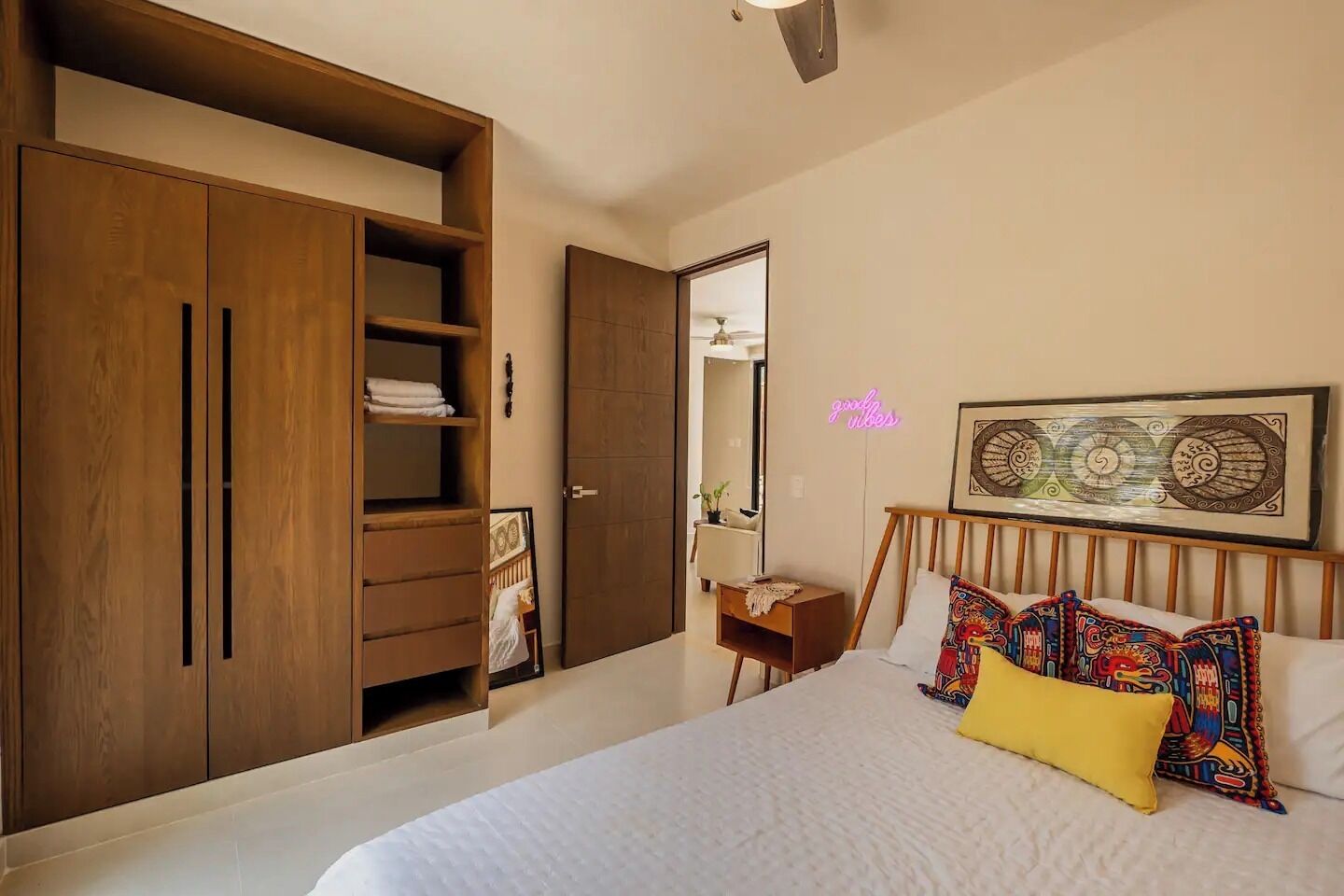 Un dormitorio con un armario de madera grande, una cama con almohadones coloridos y una obra de arte colgada en la pared.