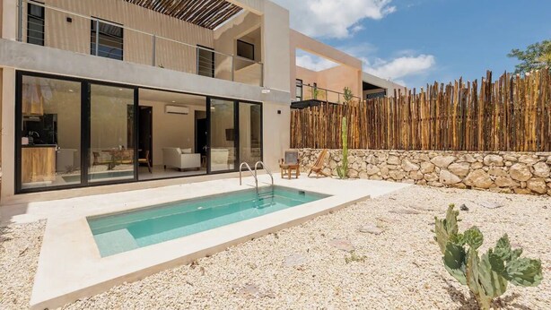 A modern two-story house with a swimming pool, stone wall, and cactus plants. - Beautiful 2 Bedroom Apartment (Tulum)