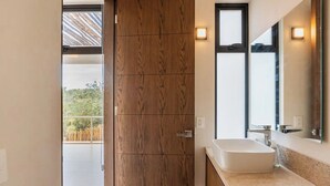 A modern bathroom with a large window, a wooden door, and a large mirror. - Beautiful 2 Bedroom Apartment (Tulum)