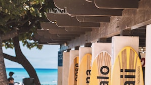 Diverse tavole da surf con la scritta "Mahalo Hawaii" disposte sotto una struttura in legno sulla spiaggia.