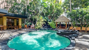 Una piscina con bordo in pietra naturale, circondata da vegetazione tropicale e mobili in legno.
