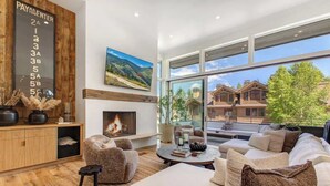 A modern living room with a fireplace, large windows, and a view of houses. - Abode at River Run, mountain modern, Ketchum (Ketchum)