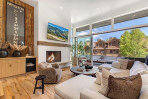 A modern living room with a fireplace, large windows, and a view of houses.