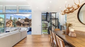 A modern interior with a wooden dining table, white sofa, and a view of a mountain cabin through large windows. - Abode at River Run, mountain modern, Ketchum (Ketchum)