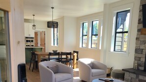 Ein modernes Wohnzimmer mit zwei Sofas, einem Couchtisch und einem Kamin. Es gibt einen Essbereich mit Tisch und Stühlen sowie eine Küche mit Schränken und Geräten.