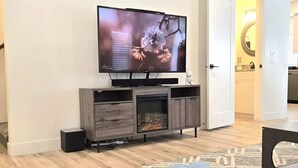 A living room with a flat-screen TV mounted on a wooden entertainment unit, a fireplace, and a sofa.