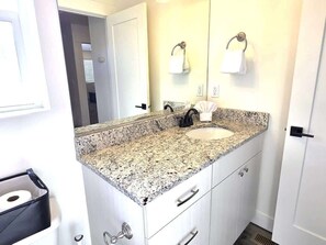 Un baño con encimera de granito, lavamanos, espejo y toallero.