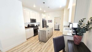 A modern kitchen with white cabinets, a central island, and a dining area with a chair and table.