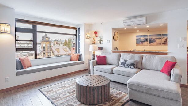 A modern living room with a sofa, a round coffee table, and a large window overlooking a building. - Moscato-Ski-In/Ski-Out (A Condo at Carleton Lodge) (Whistler)