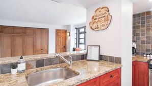 A modern kitchen with granite countertops, stainless steel sink, wooden cabinets, and a decorative wall sign. - Moscato-Ski-In/Ski-Out (A Condo at Carleton Lodge) (Whistler)