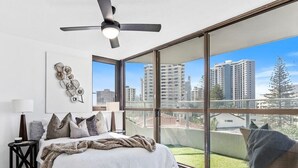 Ein Schlafzimmer mit großem Fenster, Deckenventilator und einem Bett mit Kissen.