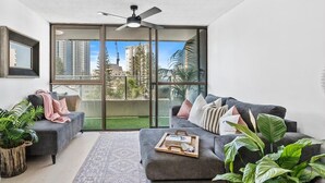 Ein modernes Wohnzimmer mit einem grauen Sofa, einem Couchtisch und einer großen Schiebeglastür, die auf einen Balkon führt.