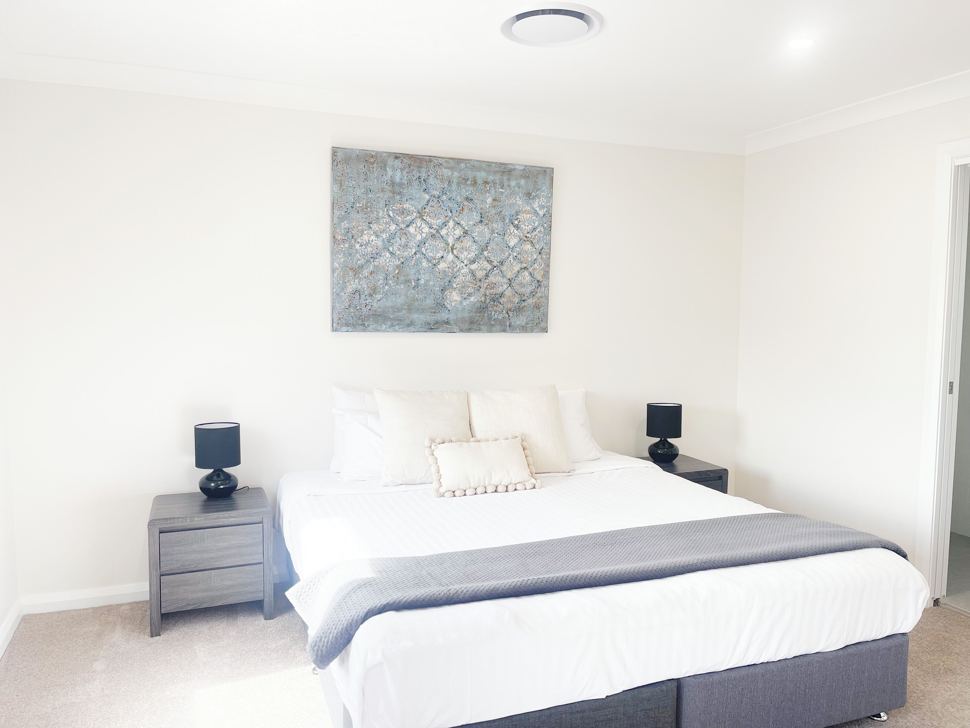 A bedroom with a bed, two bedside tables, a wall-mounted artwork, and a door.