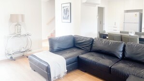 Una sala de estar moderna con un sofá de cuero negro, una mesita con una lámpara y una zona de comedor con una mesa y sillas.