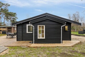 A black cabin with a wooden deck, a window, and a metal pipe.