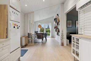 Eine moderne Küche mit weißen Schränken, eine Essecke mit Tisch und Stühlen sowie ein Ausblick durch ein großes Fenster.