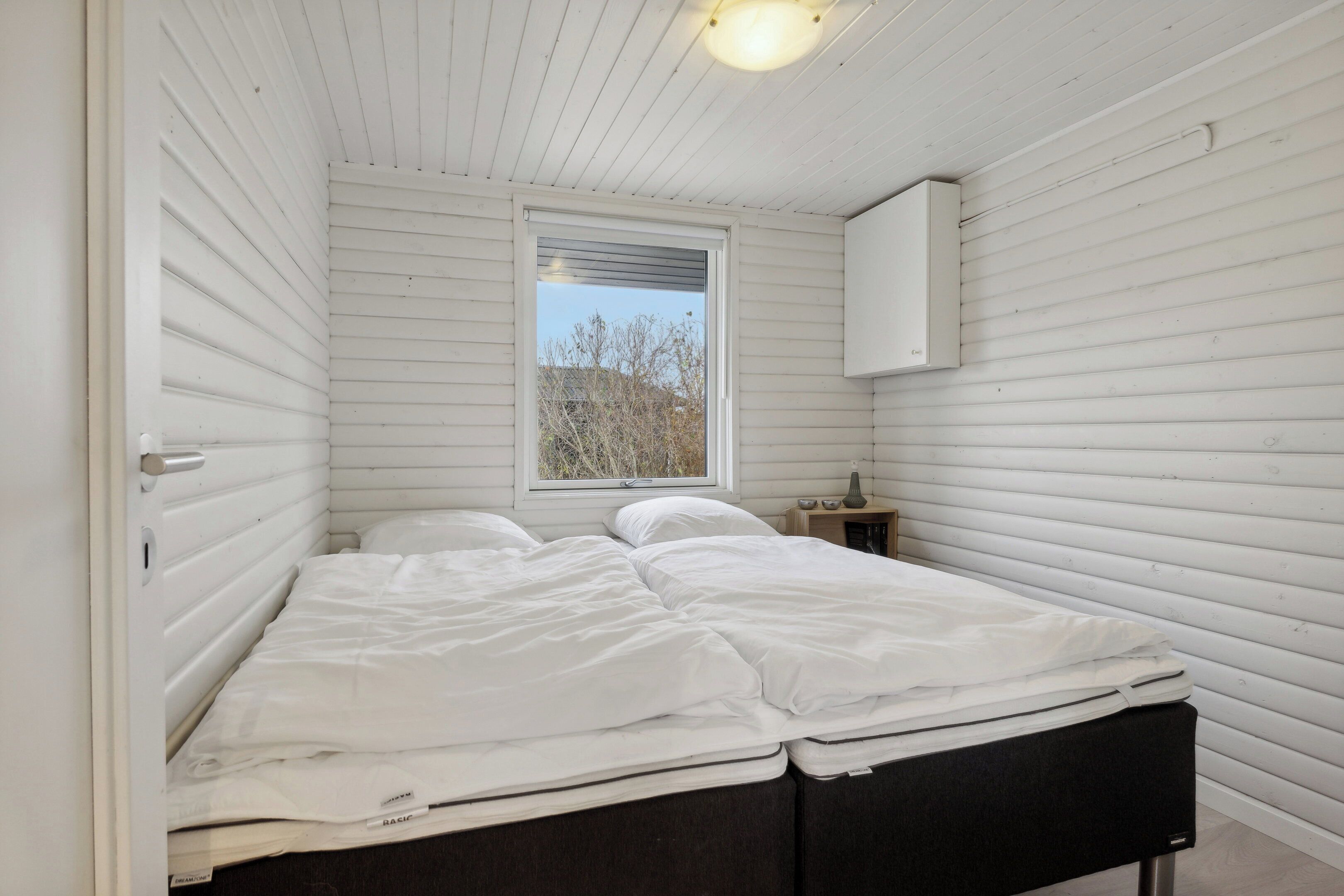 Quarto com uma cama, uma janela e uma mesinha de cabeceira.