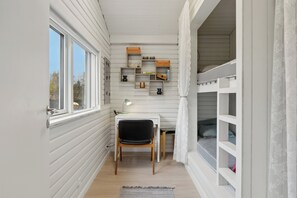 A narrow room with a desk, chair, shelves, and bunk beds.