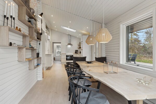 Una cocina moderna con estantes de madera, una zona de comedor con sillas e iluminación colgante.