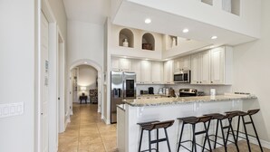 A modern kitchen with white cabinetry, a central island with bar stools, and a microwave above the island. - Coastal Retreat – Near the Beach w/ Private Hot Tub & Spacious Backyard Oasis (Indian Harbour Beach)