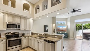 A spacious kitchen with white cabinetry, stainless steel appliances, and a granite countertop. - Coastal Retreat – Near the Beach w/ Private Hot Tub & Spacious Backyard Oasis (Indian Harbour Beach)