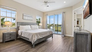 A bedroom with a bed, nightstands, a ceiling fan, and large windows with a view. - Coastal Retreat – Near the Beach w/ Private Hot Tub & Spacious Backyard Oasis (Indian Harbour Beach)