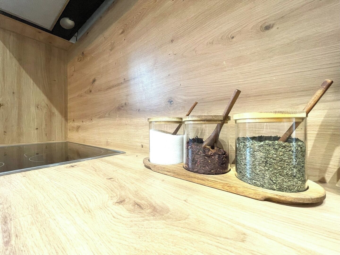 Un comptoir de cuisine en bois sur lequel reposent trois bocaux en verre contenant différentes substances, chacun accompagné d’une cuillère en bois.