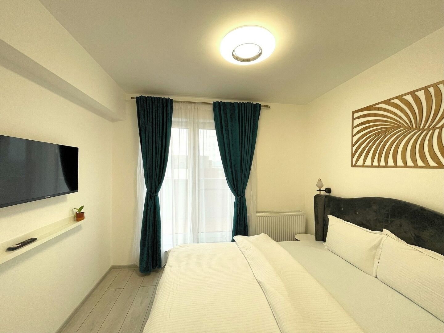 Ein Hotelzimmer mit einem Bett, einem an der Wand montierten Fernseher, einem Heizkörper und einer Wanddekoration.