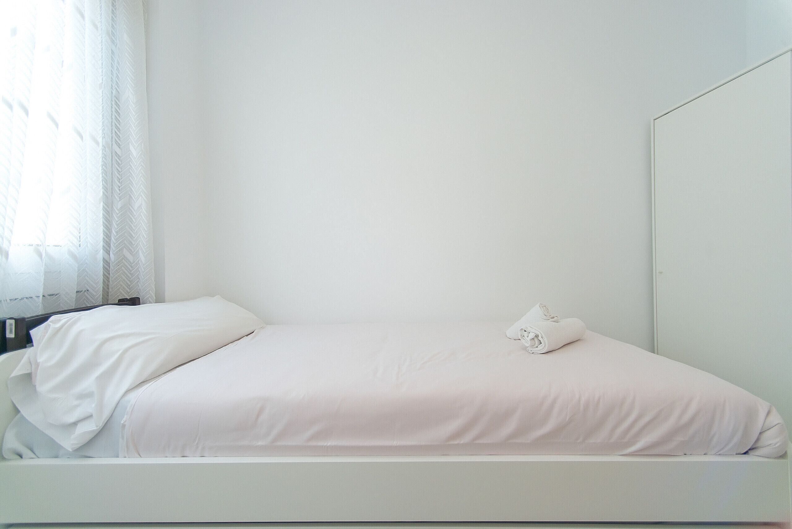 Un dormitorio minimalista con cama, mesita de noche y espejo.