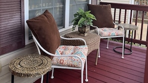 Une véranda avec deux fauteuils en osier, une petite table ronde et un pot de fleurs.