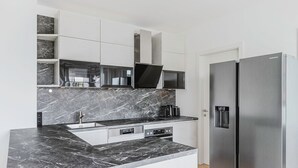 A modern kitchen with a black marble countertop, stainless steel appliances, and white cabinetry. - Blueground | Donaustadt, furnished & ready (Vienna)