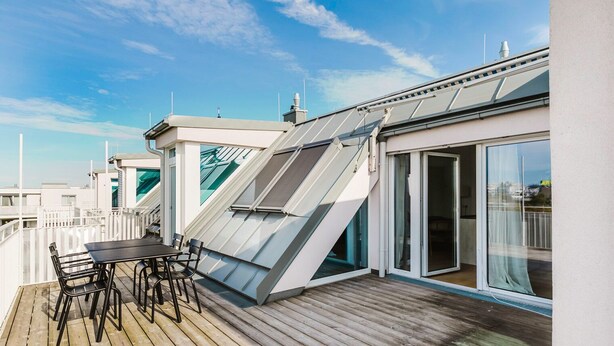 A rooftop deck with a table and chairs, a sliding glass door, and a sloped roof with skylights. - Blueground | Donaustadt, furnished & ready (Vienna)