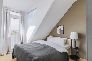 Een moderne hotelkamer met een groot bed, een bedlampje en een stadszicht door een groot raam.