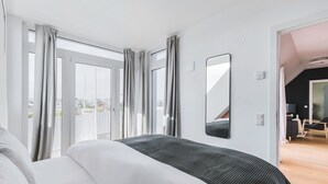 A modern hotel room with a large bed, a balcony with curtains, a flat-screen TV, and a small seating area. - Blueground | Donaustadt, furnished & ready (Vienna)