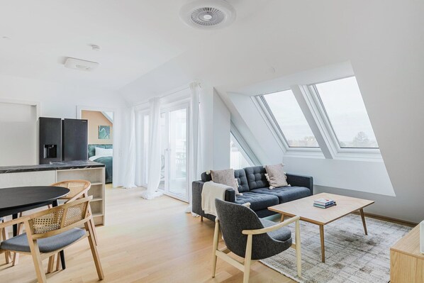 Een modern appartement met keuken, eetgedeelte en woonkamer. Het heeft een groot dakraam, een bank en een eettafel.