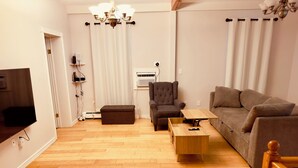 Een woonkamer met een bruine bank, een houten salontafel, een bruine fauteuil en een televisie op een meubel.