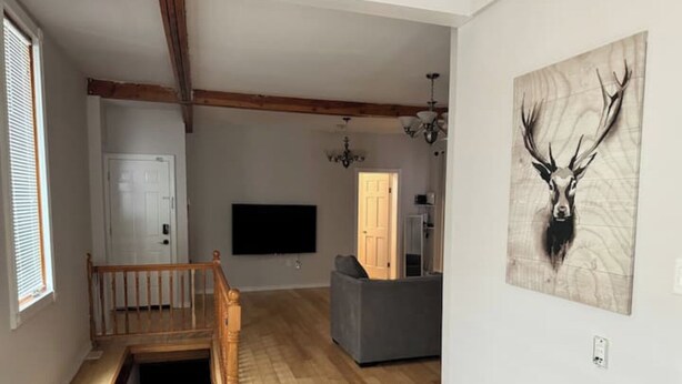 Een ruime woonkamer met een houten trap, een flatscreen televisie en een kunstwerk van een herten aan de muur.