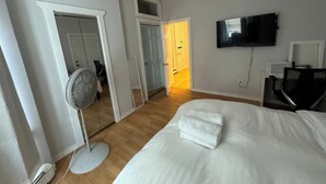 Een hotelkamer met een bed, een aan de muur bevestigde televisie, een ventilator en een deur naar een andere kamer.